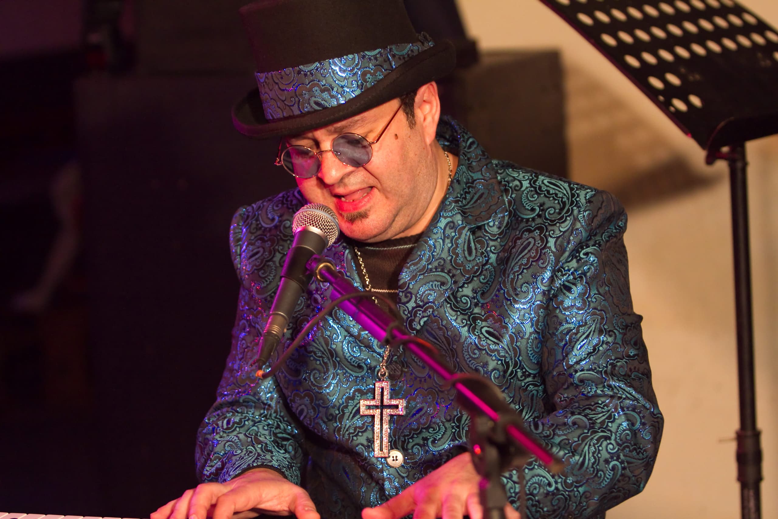 Dragoș performing as Elton John at the piano, wearing a top hat, round tinted glasses and a paisley stage jacket