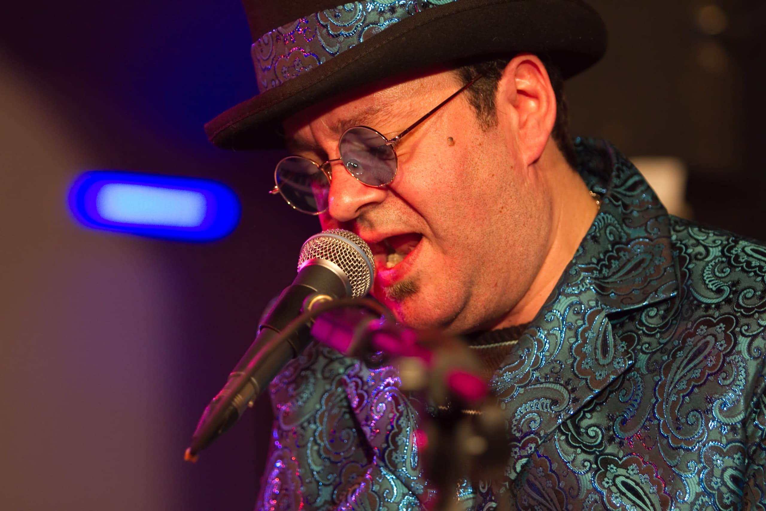 Mid-song close-up of the performer singing into the microphone under blue stage light