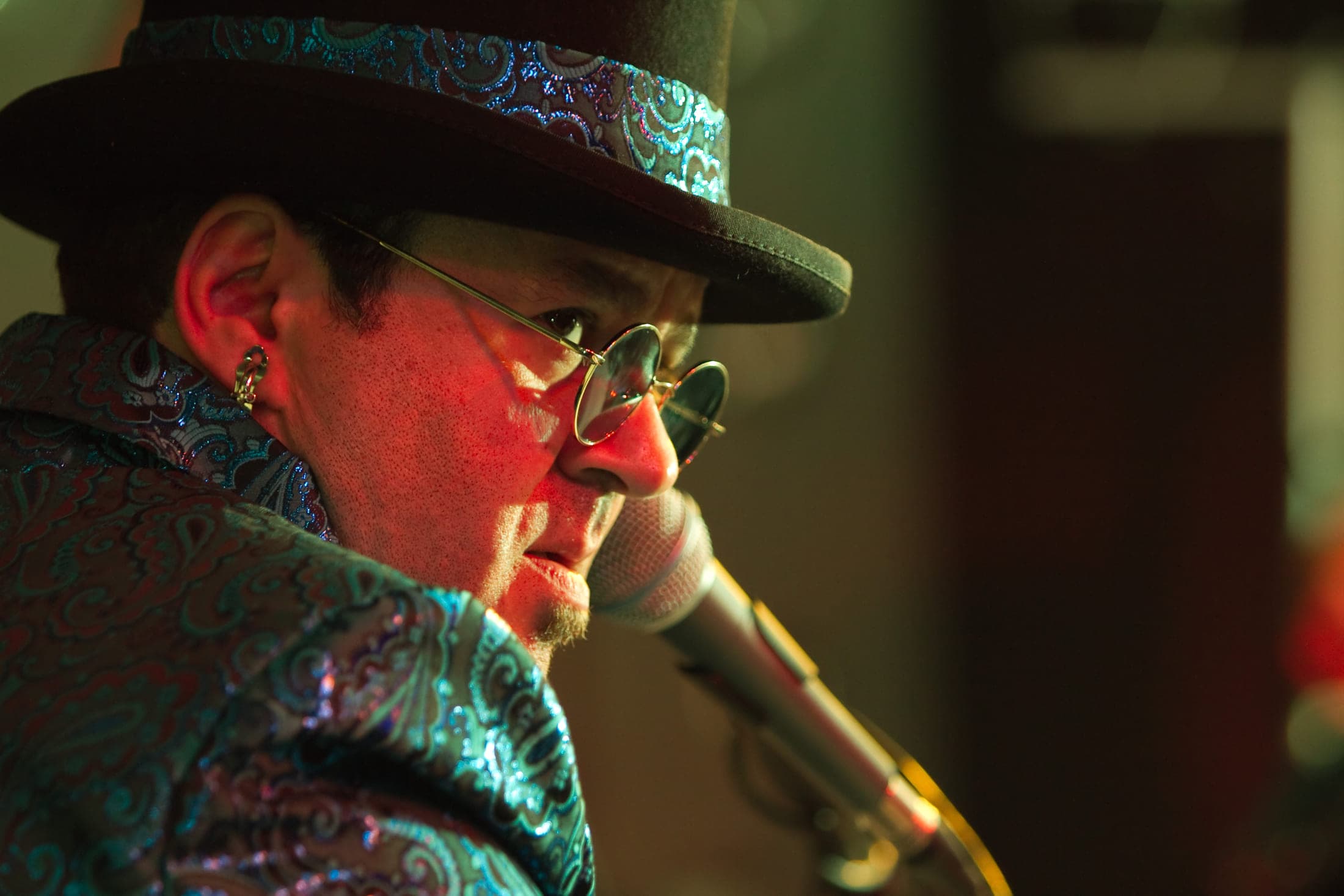 Close profile portrait of the performer in a top hat and round glasses at the microphone