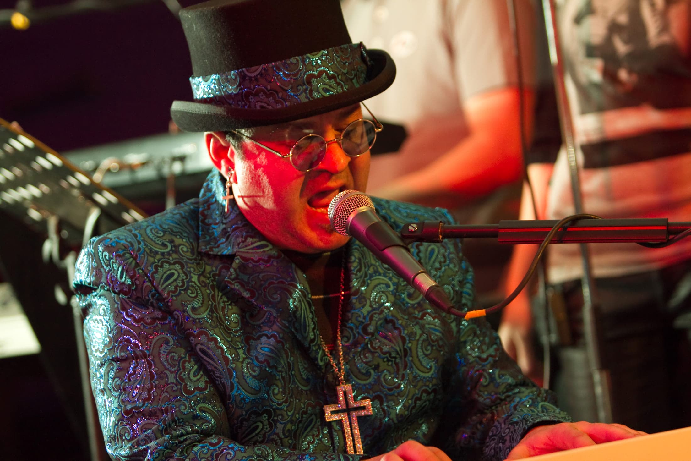 The performer singing into the microphone at the keyboard under warm red stage lighting